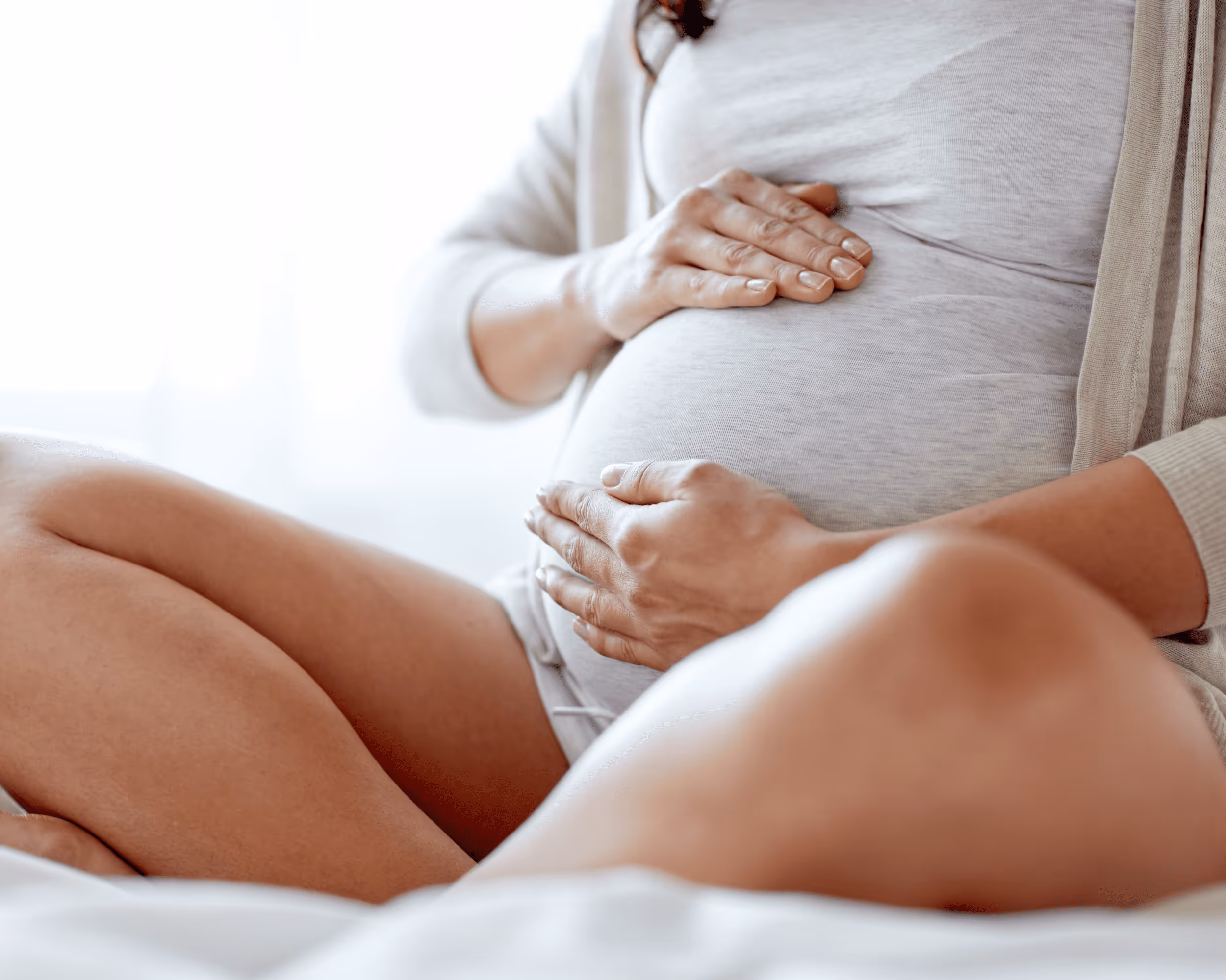 Schwangere Frau legt beide Hände auf ihren Bauch.